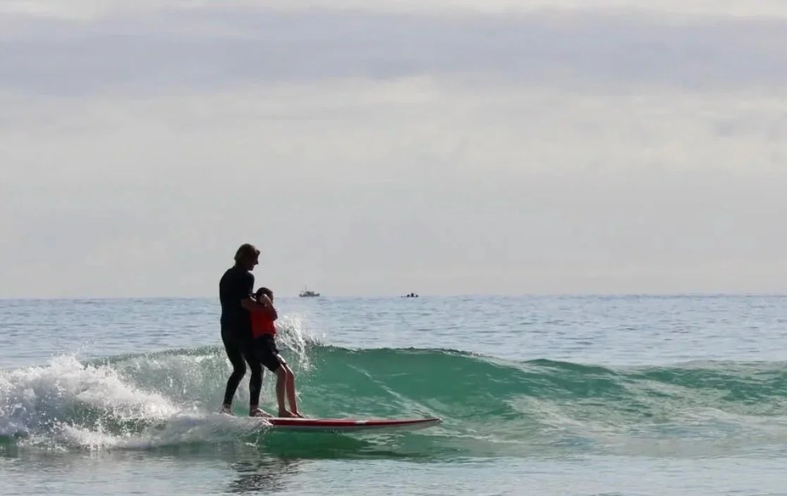 A volunteer surfing a wave with a child at Waipu Cove